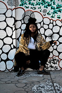 woman in brown and black leopard print coat leaning on white and black wall thumbnail