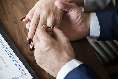 person putting gold-colored wedding band on woman's hand thumbnail