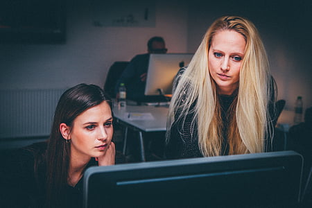 two women staring in black monitor in dim-lighted room thumbnail