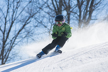 person wearing green ski jacket and snow goggles skiing over snow ground with distance at bare trees during daytime thumbnail