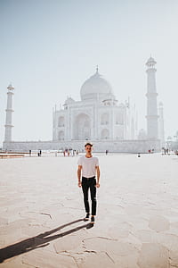 white concrete dome church behind man wearing white t-shirt and black pants standing on ground during daytime thumbnail