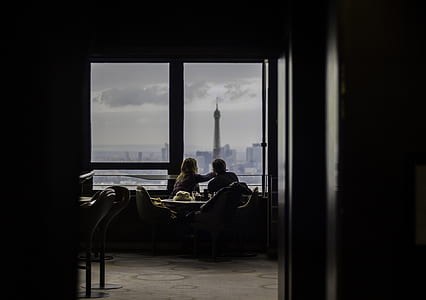 man and woman facing tower while sitting in front of window thumbnail