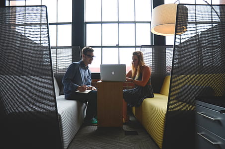 Smiling Man and Woman Both Sitting on Sofa Both Looking at Silver Macbook thumbnail