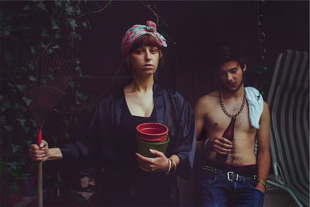 woman holding brown and red rake and two pots standing beside man holding open bottle thumbnail