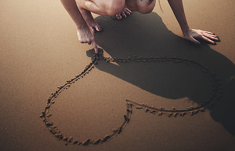 woman drawing heart shape on beach sand thumbnail