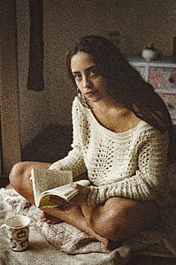 woman wearing white sweatshirt sitting in the bed while holding a book thumbnail