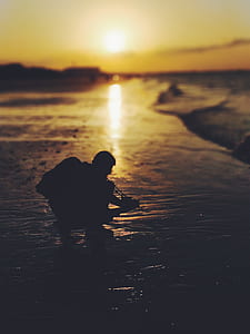 silhouette photography of man sitting on shoreline thumbnail