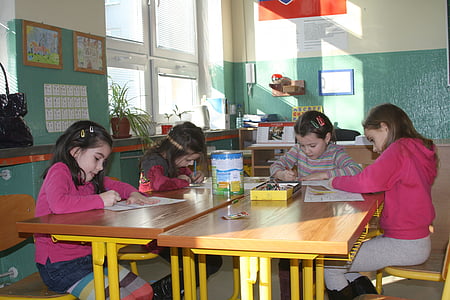 girls holding coloring materials while sitting on chair thumbnail