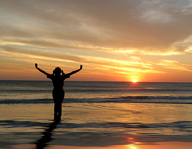 silhouette photo of a woman spreading her hands near seashore during golden hour thumbnail