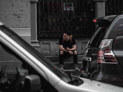 man sitting on stairs near vehicle son road thumbnail
