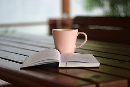 close-up photo of white labeled book open beside pink ceramic coffee mug on brown wooden table thumbnail