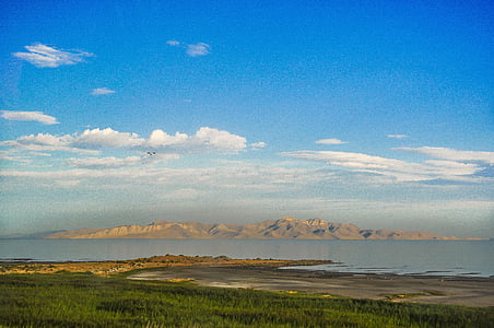 landscape photography of brown hills across calm body of water with distance at green trees under blue cloudy sky thumbnail