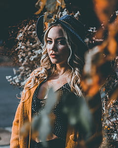 woman in brown coat and blue hat surrounded by white flowers near body of water at daytime thumbnail