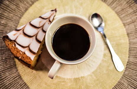 black liquid filled in white ceramic mug in between sliced cake and teaspoon thumbnail