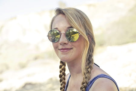 A young blonde woman wearing blue tank top and sunglasses posing outdoors thumbnail