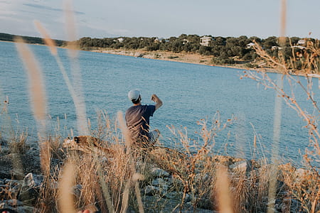 person in brown shirt sitting and facing body of water thumbnail