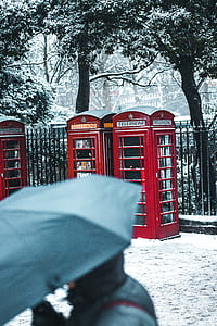 three red telephone booths near fence taken during winter time thumbnail