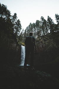 man standing on cliff facing waterfalls thumbnail