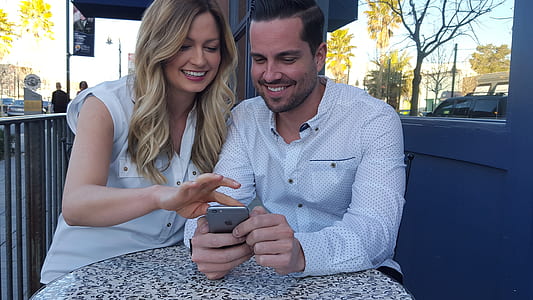 man using iPhone beside woman sitting near road thumbnail