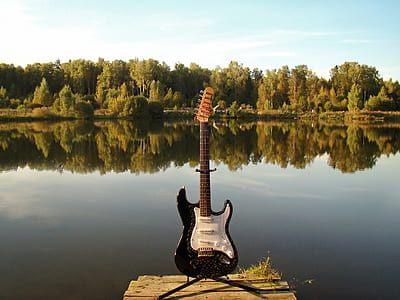 white and black electric guitar standing upright in front of body of water thumbnail
