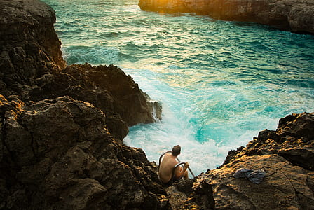 man sitting on rocks in front of body of water thumbnail