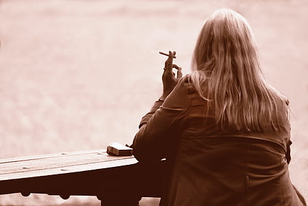 woman wearing brown jacket sitting by the table while smoking thumbnail
