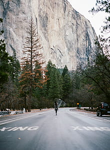 person walking at the middle of the road towards mountain thumbnail
