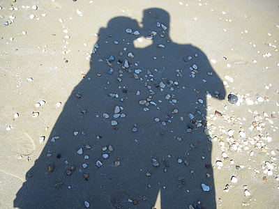 shadow of couple kissing viewed on gray sands on shore with assorted stones during daytime thumbnail