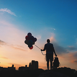 silhouette photo of person holding balloons and bag during golden hour thumbnail