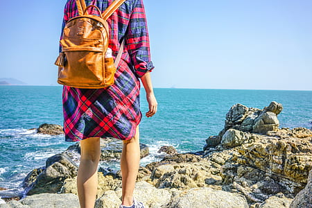 woman wearing backpack standing beside stone near at water thumbnail