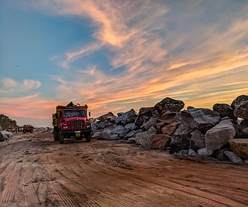 Red Dump Truck Near Filed Rocks Under Cloudy Sky thumbnail