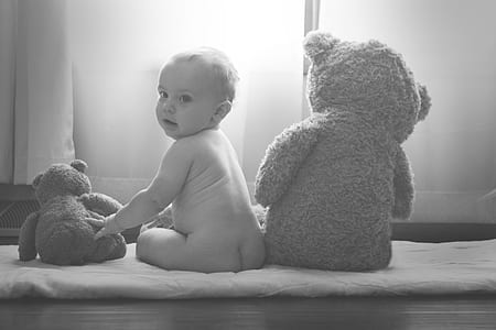 grayscale photo of naked baby sitting next to two teddy bears thumbnail