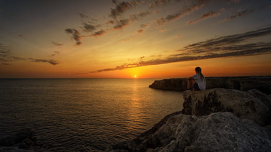 woman sitting on rock near seashore during sunset thumbnail