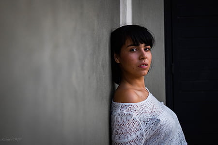 woman wearing white top leaning her back on gray wall thumbnail