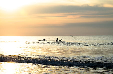 two people surfing on sea during golden hour thumbnail