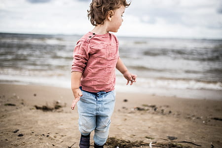 boy wearing pink sweatshirt and gray denim jeans on sand near ocean thumbnail