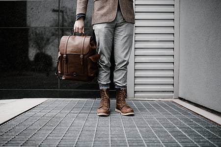person holding brown leather backpack near gray and black wall thumbnail