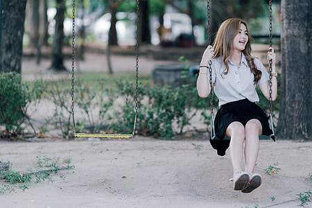 selective focus photography of woman wearing gray button-up collared shirt and black skirt sitting in metal framed swing thumbnail