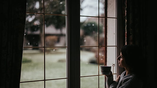 woman holding mug looking through glass window thumbnail