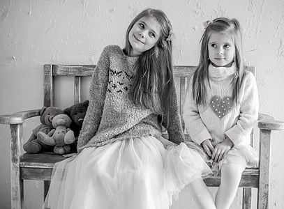 grayscale photo of two girls sits on bench chair with teddy bears thumbnail