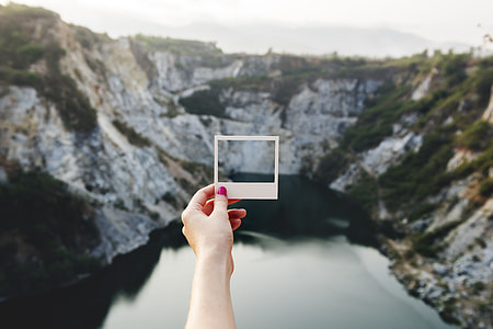 person holding photo paper in front of gray and brown mountains thumbnail