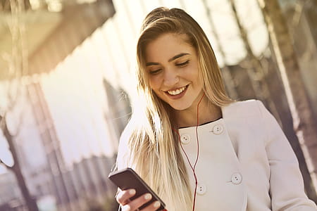 Young Blonde Woman Wearing White Buttoned Coat Using Smartphone To Listening To Music thumbnail