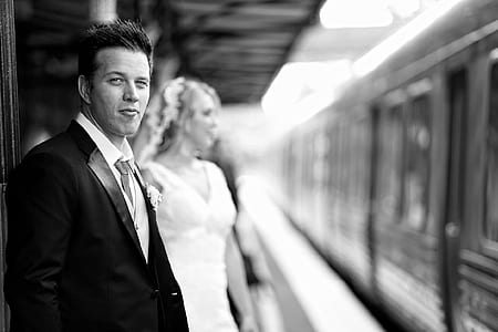grayscale photography of standing man beside his bride near train thumbnail
