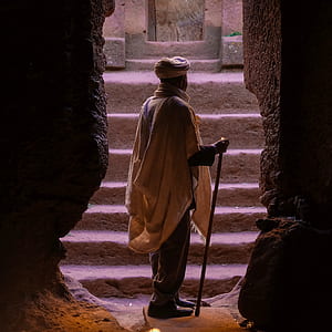 man wearing beige tuban standing between cave thumbnail