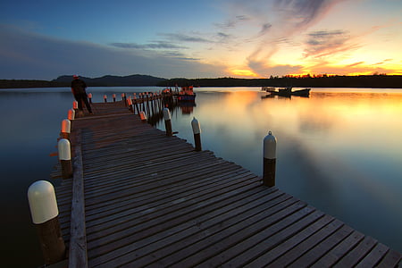 person standing on brown wooden dock during sunset thumbnail