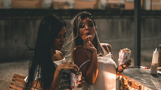 two woman eating popcorn beside picnic table thumbnail