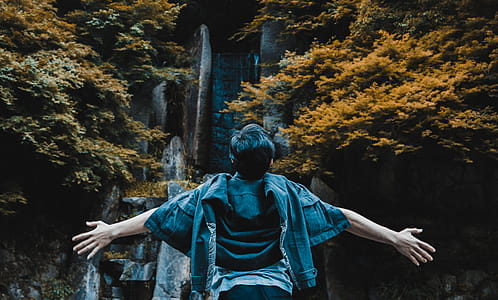 Person Spreading His Hands in Front of Gray Concrete Structure Surrounded by Brown and Green Leaf Trees thumbnail