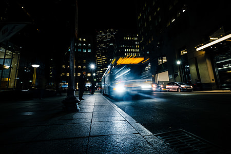 man standing beside bus in front of post overlooking high-rise buildings during nightime thumbnail