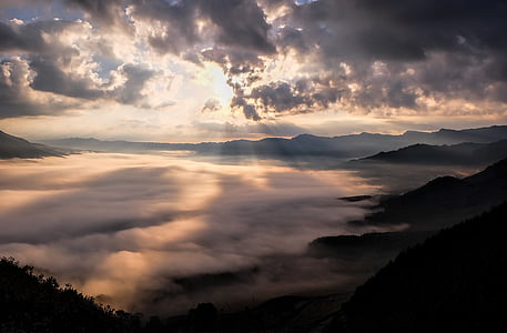 landscape photography of sea of clouds surrounded by mountains with crepuscular sun rays with cloudy sky thumbnail