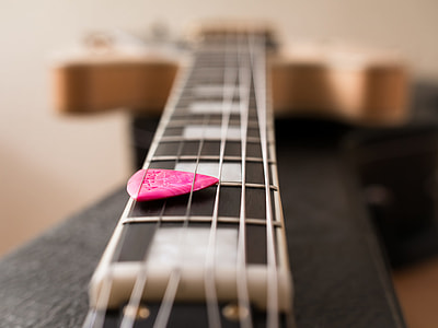 tilt shift photography of pink guitar pick on black guitar thumbnail